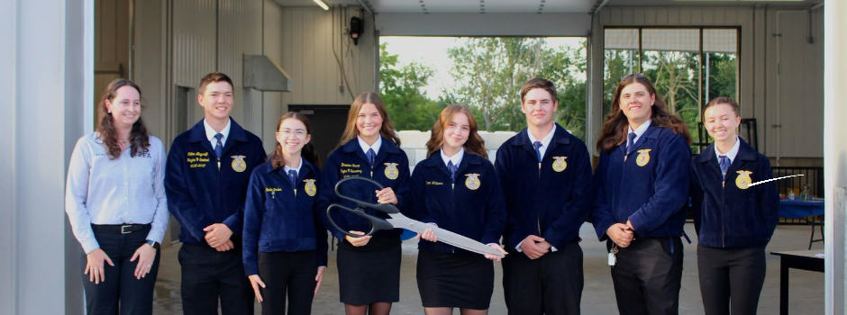 Coopersville FFA students and their advisor stand inside the new FFA barn holding ceremonial ribbon-cutting scissors.