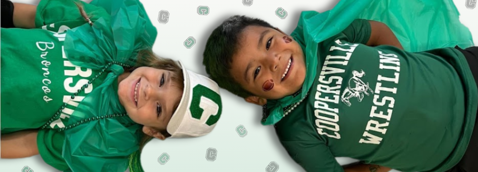 Two young children in green Coopersville Bronco shirts and capes lying on the floor smiling, with Bronco beads and a ‘C’ visor hat.